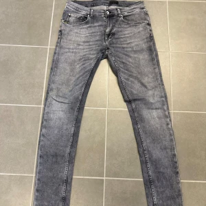Grå jeans från Tiger of Sweden - Snygga grå jeans från Tiger of Sweden. Klassisk femficksmodell, silverfärgade nitar och knapp, samt diskret logga på fickan. Jeansen har en tvättad look och är tillverkade i stretchig bomullsdenim för en bekväm känsla.