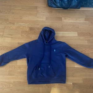 Marinblå hoodie från Polo Ralph Lauren - Säljer en marinblå hoodie från Polo Ralph Lauren med klassisk broderad logga på bröstet. Tröjan har huva med snörning, känguruficka och långa ärmar. Skön och stilren modell i mjuk bomullsblandning, perfekt för chill dagar. Den är dock väldigt liten i storleken den är typ XS/S