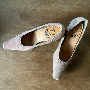 Beige mocka klackskor - Snygga pumps i beige mocka med markerad fyrkantig tå och diskreta nitar vid öppningen. Skorna har en stadig klack i trälook och är tillverkade i äkta skinn för en lyxig känsla. Perfekta för dig som gillar klassisk stil med en twist.