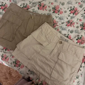 Två korta cargokjolar från Lager - Två cargokjolar från Lager 157, en i beige och en i ljusbrun. Båda har stora fickor framtill, knapp och dragkedja. Perfekt för en avslappnad och trendig look. Snygga att matcha med crop tops eller hoodies. Tillsammans för 120:-