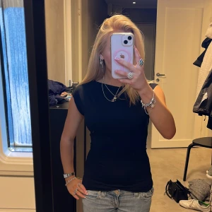 Svart ärmlös topp i stretchigt material - Säljer en svart, tight och ärmlös topp med rund halsringning. Toppen är figurnära och har en enkel, stilren design som passar till jeans eller kjol. Materialet känns mjukt och stretchigt, vilket gör den bekväm att bära hela dagen.