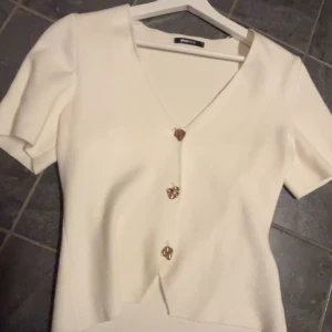 Vit topp , Gina tricot  - Säljer denna söta topp från Gina tricot , med fina guld detaljer , aldrig använd , helt som ny, storlek S, jättemjukt material