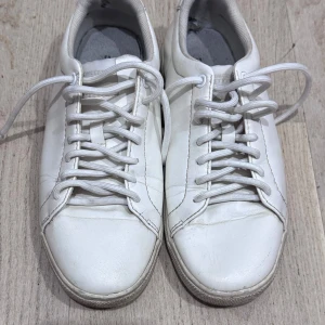 HM dividend Vita klassiska sneakers - Säljer ett par stilrena vita sneakers med rund tå och snörning. Skorna är tillverkade i skinn och har en platt sula, perfekt för en clean och enkel look. Passar till det mesta och är ett måste i garderoben för dig som gillar minimalistisk stil.