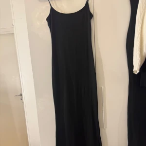 Svart långklänning med smala axelband - Enkel och stilren svart långklänning med smala axelband och rak passform. 