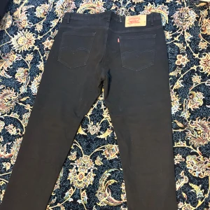 Svarta Levi's 511 jeans - Svarta Levi's 511 jeans med klassisk femficksdesign och raka ben. Jeansen har en snygg, smal passform och är tillverkade i mjukt bomullstyg med lite stretch för extra komfort. Perfekta för dig som gillar en stilren look med ikonisk Levi's-detalj på bakfickan.