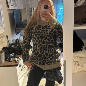 Beige leopardmönstrad stickad tröja - Säljer en beige stickad tröja med svart leopardmönster och bred polokrage. Tröjan har ribbade muddar vid ärmslut och nederkant, samt lång ärm. Perfekt för dig som vill sticka ut med ett djurmönster i höst och vinter.