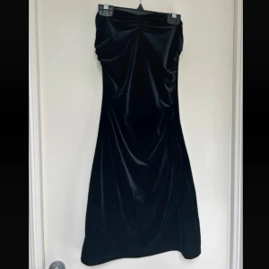 Svart sammetsklänning från Bik Bok - Supersnygg svart långklänning i sammet från Bik Bok. Axelbandslös modell med figurnära passform och lätt rynkdetalj upptill. Perfekt för dig som vill ha en elegant och stilren look med lyxig känsla.