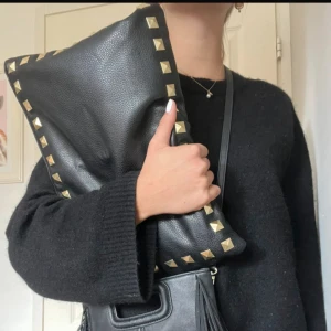 Svart datorfodral med nitar - Stor svart datorfodral  i skinn med coola guldfärgade nitar längs kanterna. Väskan har en stilren och edgy look, perfekt för att lyfta vilken outfit som helst. Mjuk struktur och rymlig insida, lätt att bära under armen.