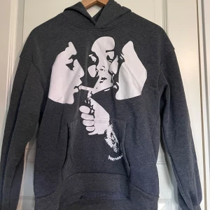 Graphic hoodie - Säljer en mörkgrå hoodie med ett stort vitt grafiskt tryck på framsidan som föreställer tre ansikten och en hand. Storlex: XS/S