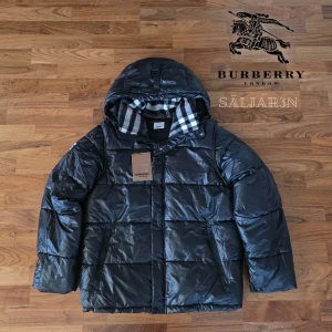 Burberry Puffer - Svart dunjacka från Burberry med klassisk Säljer en elegant och mångsidig Burberry-jacka i svart, i nyskick. Dunfodrad för värme och komfort med det klassiska rutmönstret i huvan som ger en exklusiv touch. Praktiska dragkedjefickor, avtagbar huva och diskret logopatch på ärmen. Sitter som (M/L). Jackan är i princip som ny och utan defekter. En lyxig kombination av stil och funktion – perfekt för både vardag och tillfällen då du vill klä upp dig.  📦Snabb leverans - skickas samma dag📦 