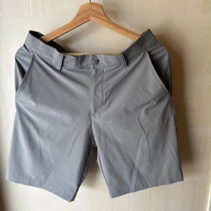 Grå golfshorts från Adidas i storlek 30 - Snygga grå golf shorts från Adidas med klassisk passform och bälteshällor. De har två sidofickor fram och två bakfickor, samt diskret Adidas-logga bak. Perfekta för sommardagar och sportiga outfits. Materialet är mjukt och lätt för extra komfort.