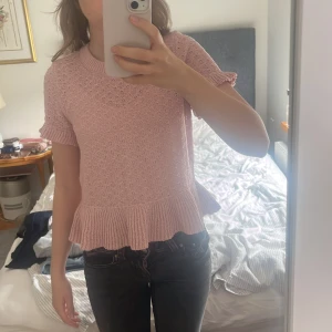 Rosa stickad topp med volang från Divided - Supersöt ljusrosa stickad topp från Divided med korta ärmar och volangkant nedtill. Toppen har rund halsringning och ett diskret strukturmönster i tyget. Perfekt för dig som gillar en feminin och trendig stil.