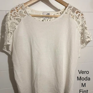 Vit blus med spetsdetaljer Vero Moda - Superfin vit blus från Vero Moda i storlek M. Toppen har korta ärmar med snygga virkade spetsdetaljer över axlarna och en rund halsringning. Perfekt för dig som gillar en romantisk och stilren look.