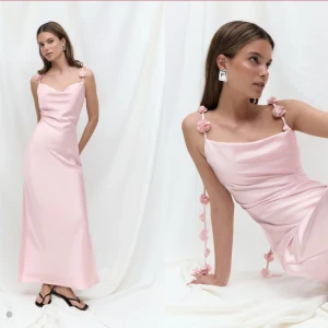 Gina tricot Ljusrosa långklänning 38 - Superfin ljusrosa långklänning i satinliknande material med smala axelband dekorerade med små tygblommor. Klänningen har en snygg draperad urringning och en elegant, figurnära passform. Perfekt för dig som vill sticka ut med en romantisk och trendig look.