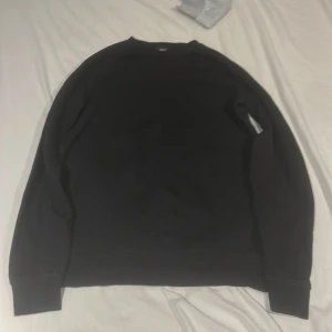 Svart sweatshirt från NEXT - En stilren svart sweatshirt från NEXT med klassisk rund hals och långa ärmar. Tröjan är i mjuk bomullsmix och har ribbade muddar vid ärmslut och nederkant. Perfekt för en avslappnad och enkel look.