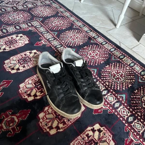 Stilrena svart vita skor från Björn Borg - Svarta sneakers från Björn Borg med vita detaljer och signatur på sidan. Skorna har snörning, rund tå och platt sula. Ovandelen är i skinnliknande material och insidan är ljusgrå. Perfekta för en avslappnad och stilren look.            Storlek 41