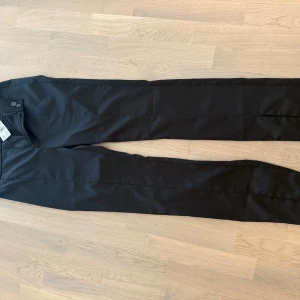 Svarta satinbyxor med slits, strl 36 bikbok - Nya.  Snygga svarta byxor i satin med slits framtill på benen. Byxorna har en rak passform och stängs med knapp och dragkedja. Perfekta för dig som vill ha en stilren look med en twist. Materialet ger en lyxig känsla och glans.  