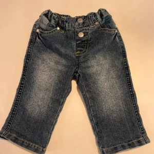 Babyjeans med broderi från Lindex - Söta blå babyjeans från Lindex med resår i midjan och broderad text 'little rock star' samt en gul stjärna på bakfickan. Jeansen har klassisk femficksdesign, kontrastsömmar och mjukt denimtyg som är bekvämt för de minsta.