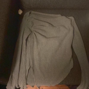 Ribbad grå långärmad tröja - Mysig ribbad tröja i grått med lång ärm och rund hals. Tröjan har en tight passform och är tillverkad i ett stretchigt stickat material som sitter snyggt på kroppen. Perfekt för lager-på-lager under kyliga dagar.