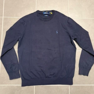 Mörkblå tröja från Polo Ralph Lauren - Mörkblå långärmad tröja från Polo Ralph Lauren i slim fit med rund halsringning. Tröjan är tillverkad i mjuk pima bomull och har den klassiska broderade loggan på bröstet. Perfekt för en clean och stilren look.