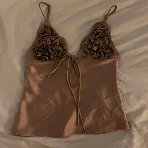 satintopp Zara - Supersnygg brun linnetopp från Zara i satin material. Toppen har smala axelband o volangdetaljer. Storlek xs/s