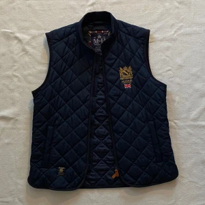 Morris Quiltad Väst - En riktigt snygg och klassisk quiltad väst från Morris. Med en tidlös design och otroligt snygga detaljer är den given i garderoben. Den har en riktigt bra passform i storlek M och fungerar perfekt till finare tillfällen men även till vardagen. Västen är i mycket bra skick! Vid intresse är det bara att höra av sig ;)