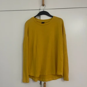 Gul långärmad tröja från Monki - En enkel och snygg gul långärmad tröja från Monki. Tröjan har rund halsringning, rak passform och är tillverkad i mjuk bomullsmix. Perfekt att styla med jeans eller kjol för en färgklick i garderoben.