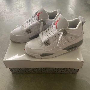 Nike Air Jordan 4 White Oreo - Nike Air Jordan 4 White Oreo med vit ovandel i skinn, meshpaneler och grå detaljer med stänkmönster. Röd Jumpman-logga på plösen och grå logga på hälen. Klassisk siluett med snörning och platt sula. Perfekta för dig som vill sticka ut med stilrena sneakers.