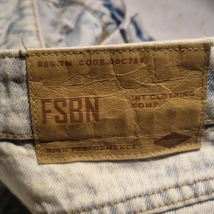 Ljusblå acid wash jeans från FSBN - Säljer ett par ljusblå acid wash jeans från FSBN med klassisk femficksdesign och raka ben. Jeansen har en cool tvättad look och är tillverkade i bomull. Perfekta för dig som gillar en avslappnad och trendig stil.
