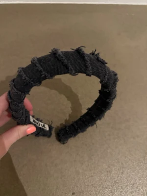 Svart denimdiadem från lexi uf.  - Trendigt svart diadem från lexi uf  i denimtyg med råa, fransiga kanter och snurrad design. Perfekt accessoar för att ge din look en edgy och cool touch. Tjock och vadderad modell som sitter bekvämt på huvudet.