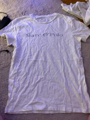 Vit t-shirt från Marc O'Polo - Klassisk vit t-shirt från Marc O'Polo med tryckt logga över bröstet. Tillverkad i mjuk ekologisk bomull och har en normal passform med korta ärmar och rund hals. Perfekt basplagg för alla tillfällen.