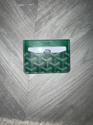 Grön goy4rd  - Snygg grön korthållare  med klassiskt mönster och guldfärgad logga framtill. Plånboken har flera kortfack och är tillverkad i exklusivt skinn med Goy4rds  ikoniska tryck. Perfekt för dig som vill ha stilren och lyxig accessoar.Kort och Box följer med