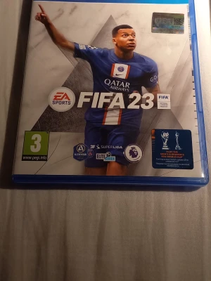 FIFA 23 & FIFA 20 till PS4 - Två fotbollsspel till PlayStation 4 och 5: FIFA 23 med blå/vit omslag och PSG-tröja samt FIFA 20 med röd/vit omslag och Real Madrid-tröja. Båda spelen har officiella ligaloggor och är perfekta för fotbollsfans som gillar att spela med vänner.