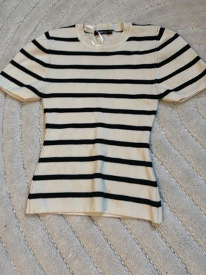 Randig ribbad topp från Gina tricot! - Snygg ribbad topp från Gina tricot  i vitt med svarta horisontella ränder. Modellen har korta ärmar och rund halsringning. Perfekt att styla med jeans eller kjol! Passar bra till allt möjligt!🌷