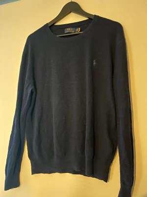 Mörkblå stickad tröja Polo Ralph Lauren - Klassisk mörkblå stickad tröja från Polo Ralph Lauren med rund halsringning och diskret broderad logga på bröstet. 