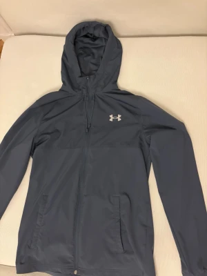Blå vindjacka från Under Armour - Använd Max 3 gånger topp skick inga skador alls, kan gå ner i pris vid snabbaffär. Jackan är Storlek S och byxorna är i M pågrund av tightare passform på byxorna.