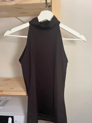 Svart ärmlös polotopp - Snygg brun polotopp i ärmlös modell. Toppen har hög hals och är figurnära med en stilren look, perfekt att matcha med jeans eller kjol. Materialet känns mjukt och stretchigt.