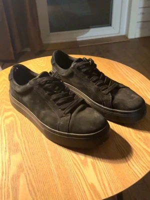 Svarta sneakers i mocka - Stilrena svarta sneakers med platt sula och rund tå. Skorna har snörning och är tillverkade i mjuk mocka som ger en snygg och modern look. Perfekta för dig som gillar minimalistisk stil och vill ha ett par klassiska sneakers till vardags.