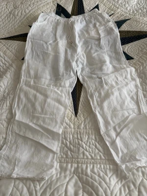 Vita linnebyxor med dragsko - Säljer ett par vita linnebyxor med avslappnad passform och elastisk midja med dragsko. Byxorna har raka ben och är perfekta för en chill och luftig stil. Inga synliga loggor eller märken. Köpte i Spanien (för ca500kr) så vet ej märke eller storlek men skulle uppskatta M. Hål i grenen! Går dock lätt att fixa.