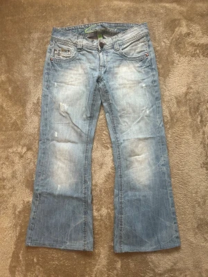 Ljusblå bootcut jeans med slitningar - Snygga ljusblå bootcut jeans med slitna detaljer. Jeansen har klassisk femficksdesign och en lätt tvättad look. Säljer då jeansen är uppsydda och blivit för korta för mig som är 165cm lång. Midjemått 82. Pris kan diskuteras