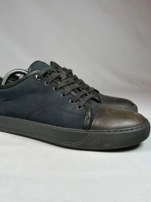 Svarta Lanvins  med skinn och textil - Stilrena svarta sneakers med ovandel i textil och tåparti i mörkt skinn. Klassisk låg modell med snörning och platt sula. Perfekta för en avslappnad och trendig look.