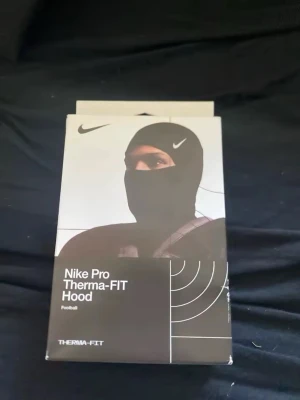 Nike Pro Shiesty Therma-FIT Hood svart - Nike Pro Shiesty Therma-FIT Hood i svart med vit Nike-logga. Tillverkad i ett tekniskt, värmeisolerande material som passar perfekt för träning utomhus. Sitter tight runt huvudet och halsen för extra värme och komfort.
