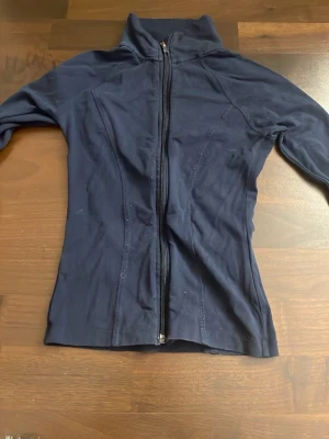 Marinblå zipjacka från Gina Tricot - Mörkblå zipjacka från Gina Tricot i storlek XS. Jackan har lång ärm, hög krage och hel dragkedja framtill. Har en slim passform som sitter snyggt på kroppen.