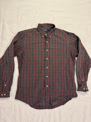 Rutig skjorta från Polo Ralph Lauren - Klassisk långärmad skjorta från Polo Ralph Lauren i rött, blått och gult rutmönster. Skjortan har knappar hela vägen, button-down krage och en liten broderad logga på bröstet. Tillverkad i bomull och har en normal passform.