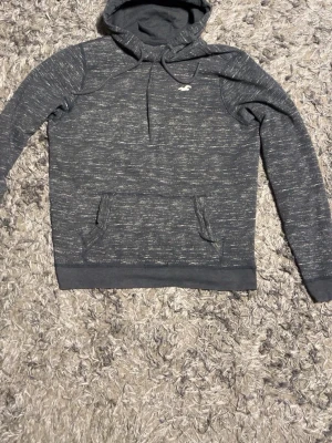 Mörkgrå Hollister hoodie – storlek L - Mörkgrå Hollister-hoodie i bekvämt material. Storlek L. Fint använt skick, hel och ren. Den är ihopsydd vid kragen 