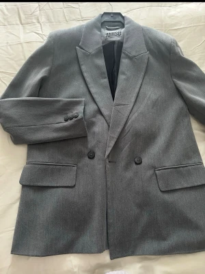 Grå kavaj från Amisu - Stilren grå kavaj från Amisu med klassisk passform och två knappar framtill. Kavajen har breda slag, två fickor med lock och tre knappar vid ärmsluten. Perfekt för en snygg och enkel look. Stor i storlek 💕💕