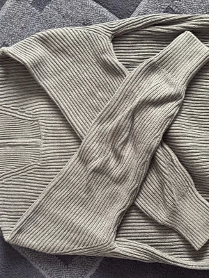 Grå ribbstickad polotröja - Säljer en stilren grå ribbstickad polotröja med hög krage och långa ärmar. Tröjan har en relaxed fit och breda muddar vid ärmslut och nederkant. Perfekt för lager på lager och enkel att matcha med olika outfits.