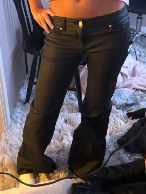 Svarta bootcut skinnbyxor med lågmidja  - Snygga svarta skinnbyxor med bootcut passform och låg midja.  knappgylf och är tillverkade i ett stretchigt byxmaterial som ger en skön och smickrande siluett.