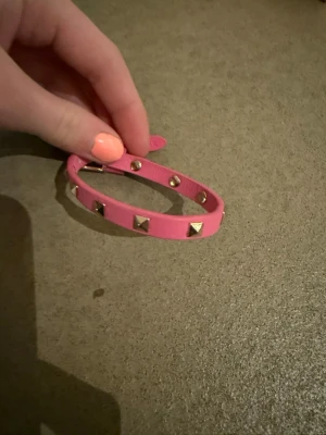 Rosa läderarmband med nitar - Snyggt rosa armband i läderimitation med silverfärgade pyramidnitar runt om. Justerbar längd med tryckknappar. Perfekt accessoar för dig som gillar en edgy och trendig stil.