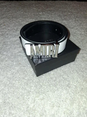 Vitt läderbälte från Amiri - Snyggt vitt bälte i läder från Amiri med en stor metallspänne där det står AMIRI. Perfekt accessoar för att lyfta din outfit med en exklusiv touch och streetwear-vibe. Bältet har stilrena sömmar och känns riktigt lyxigt.